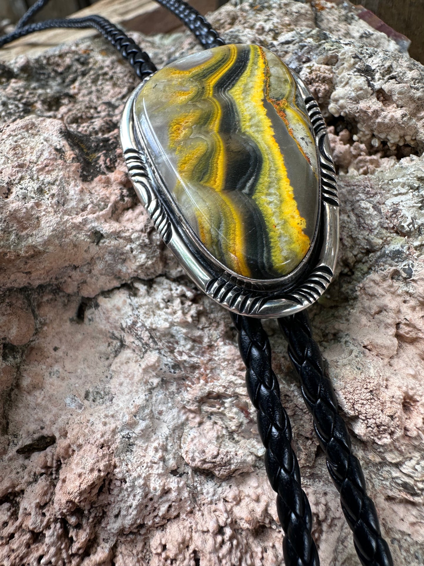 Bolo tie with a yellow and gray stone pendant on a textured rock background